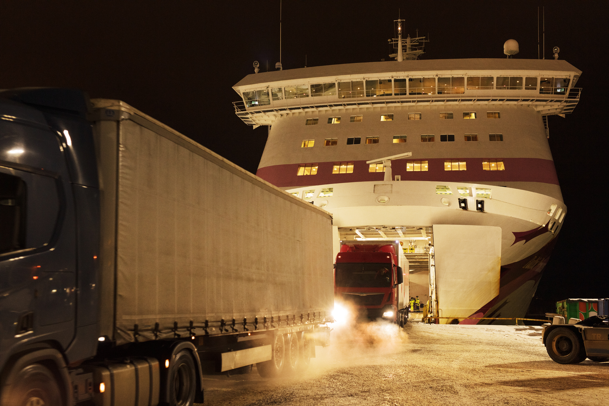 Illustration: an open cargo ship bow in the evening with trucks. 