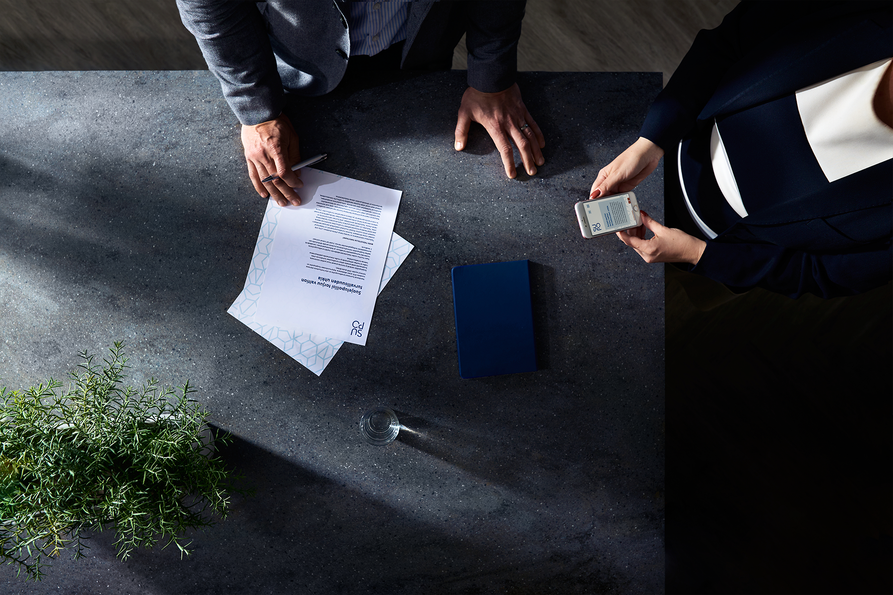  Two people by a desk, hands and papers.