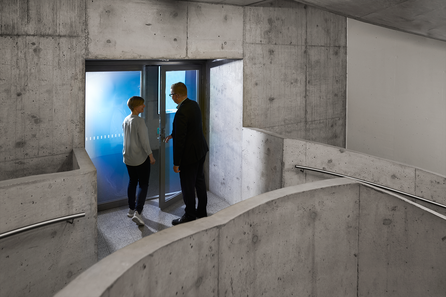 Illustration, two people at a door in a grey concrete stairway. 